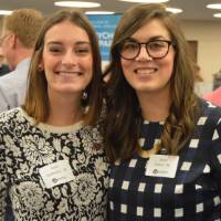 Two alumnae pose for a photo with one another at the Academic Major Fair.